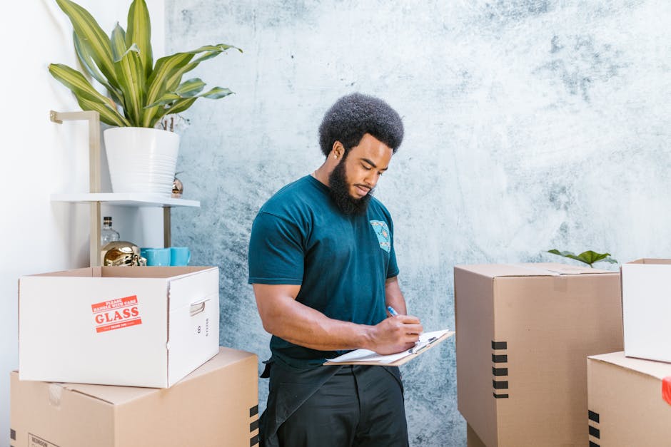 A young woman with shoulder-length blonde hair, wearing a casual green t-shirt, ripped blue jeans, and black athletic shoes with pink accents, stands indoors beside a group of unpacked cardboard boxes