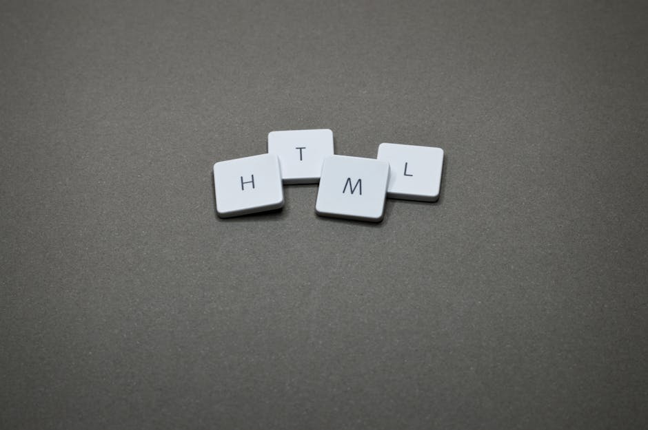 Four small white plastic tiles with black letters are arranged on a dark grey surface, spelling out the word 'HTML' with the letters H, T, M, and L clearly visible. The tiles are slightly textured, wi